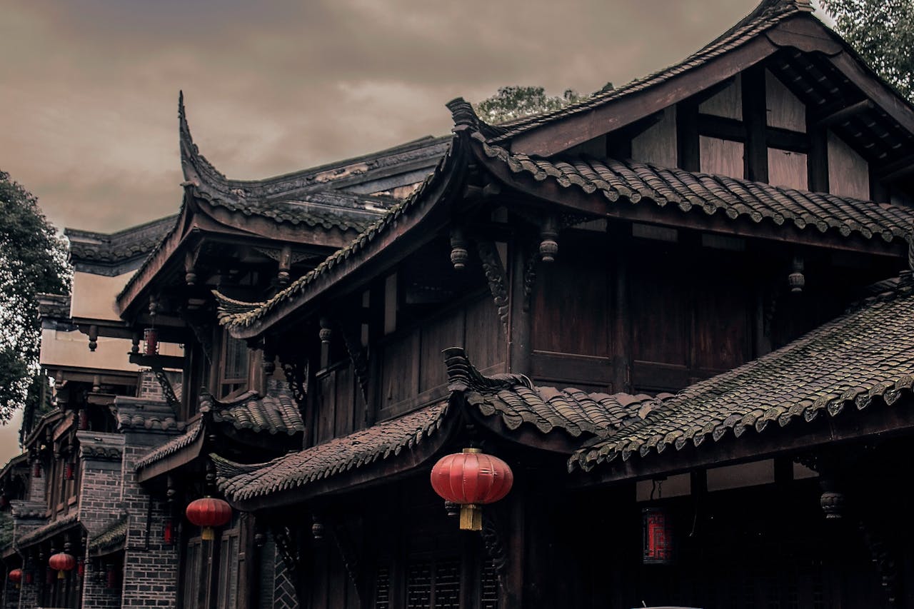 Historic Chinese building with ornate roofs and red lanterns under cloudy skies.